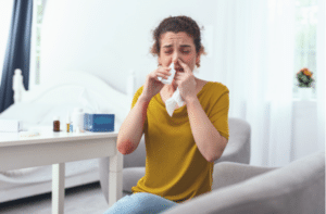 woman sitting on couch while using nasal spray for her runny nose 300x197